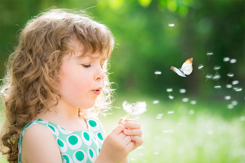 young girl blowing a dandelion