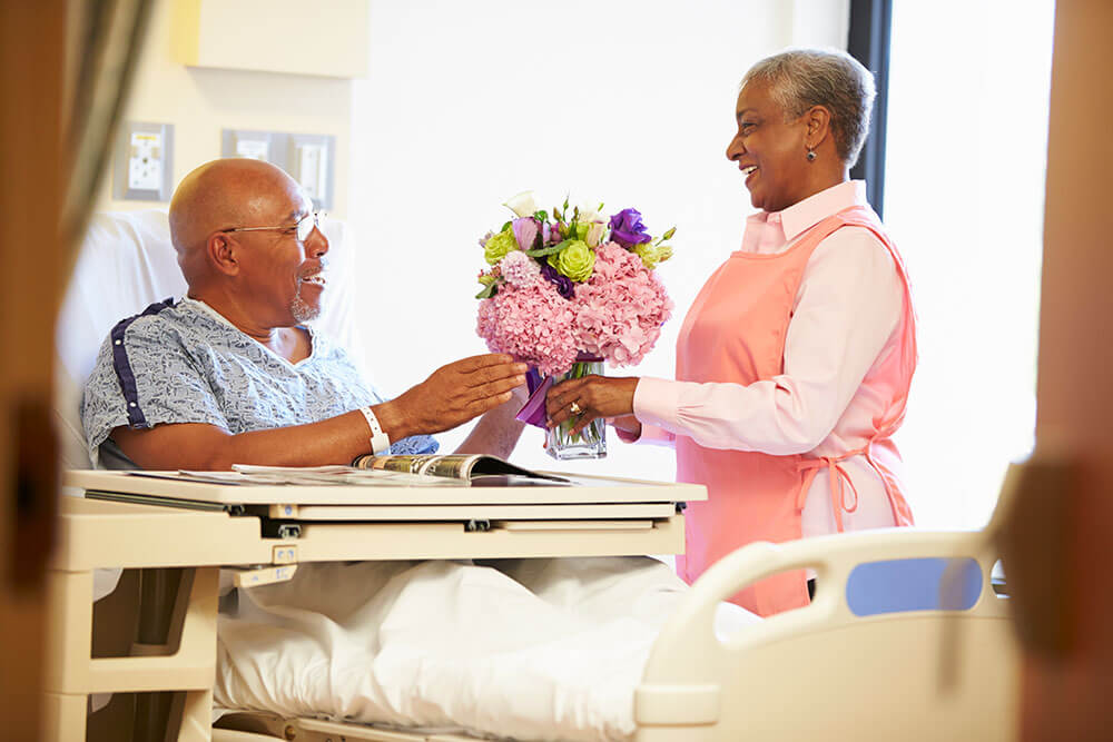 nurse handing bedridden patient a vase of flowers